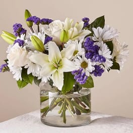 White lilies, roses, and daisies in a clear glass vase