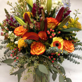Mixed bouquet of orange roses, lilies, and calla lilies in a glass vase