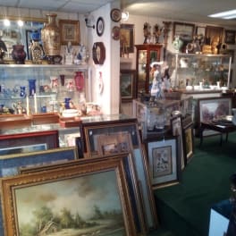 Antique shop interior with framed paintings, glass cases, and decorative vases