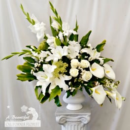 White lilies and calla lilies arranged in a white pedestal vase