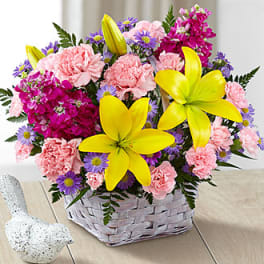 Basket arrangement of pink carnations, purple daisies, and yellow lilies