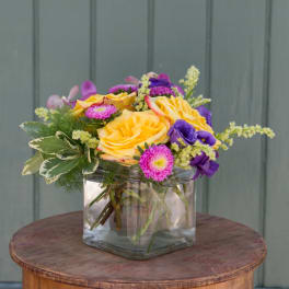 Yellow and purple flowers arranged in a clear glass vase