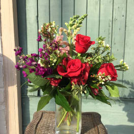 Red roses and purple flowers in a glass vase