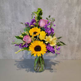 Mixed bouquet of sunflowers, roses, and purple flowers in a glass vase