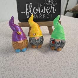 Three colorful gnome figurines displayed in front of a flower market sign