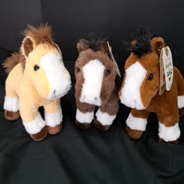Three plush horse toys on a black fabric background
