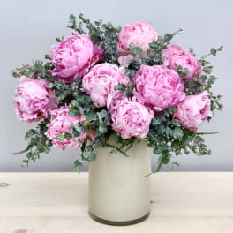 Arrangement of pink peonies with filler in a light cream cylinder vase