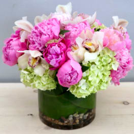 Compact arrangement of pink peonies, white orchids, and green hydrangeas in a glass vase