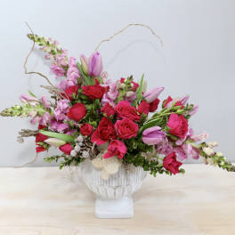 Low pink and red rose arrangement with tulips in a white pedestal bowl