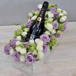 Lavender and white roses arranged around a champagne bottle in a white box