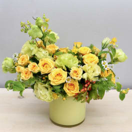 Yellow roses and green blooms arranged in a pale vase