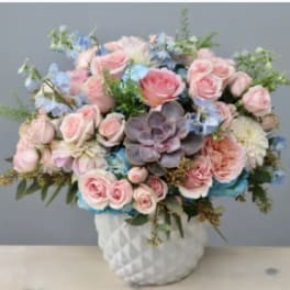 Pink roses and blue flowers arranged in a white vase with a succulent center