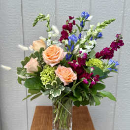 Mixed bouquet with peach roses, blue blooms, and magenta flowers in a glass vase