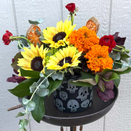 Sunflowers, orange marigolds, and red roses in a skull-patterned container