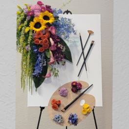 Colorful floral arrangement on a white canvas with paintbrushes and palette