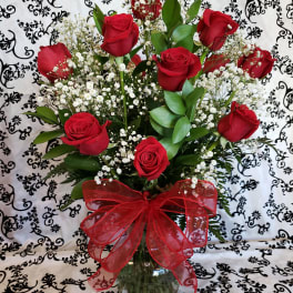 Red roses in a glass vase with baby's breath and a red bow