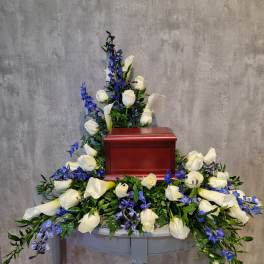 White roses and blue flowers arranged around a red urn on a table