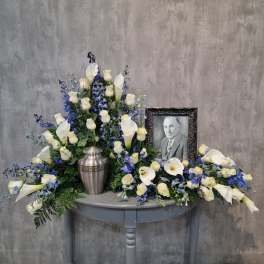 White calla lilies and roses arranged around a framed portrait and urn.