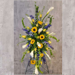 Tall standing arrangement with sunflowers, white calla lilies, and blue flowers