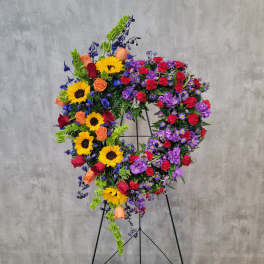Heart-shaped floral wreath on a stand with sunflowers, roses, and purple blooms