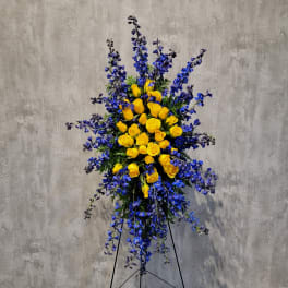 Tall standing arrangement of yellow roses and blue flowers on a black easel