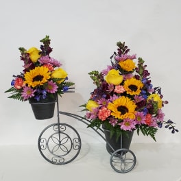 Two colorful flower arrangements in black pots on a decorative metal stand.