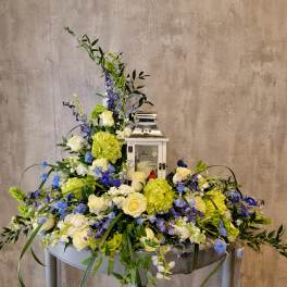 Large floral arrangement with white roses, green hydrangeas, and blue flowers around a lantern