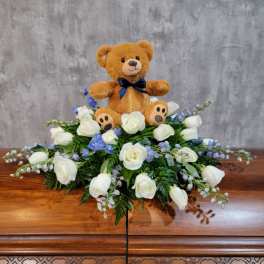 Teddy bear sitting in a white rose arrangement with blue flowers