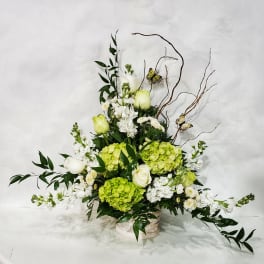 Tall floral arrangement with white roses, green hydrangeas, and butterflies in a low container