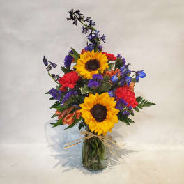 Bouquet of sunflowers, red carnations, and blue flowers in a glass vase