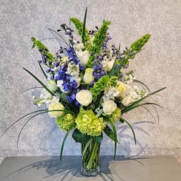 Tall bouquet of white roses, blue flowers, and green hydrangeas in a glass vase