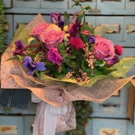 Bouquet of pink roses and purple flowers wrapped in pale paper