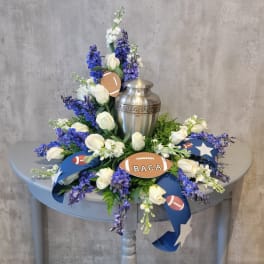 White roses and blue-purple flowers arranged around a silver urn with football decorations