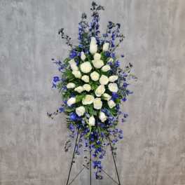 Tall standing spray of white roses and blue flowers on a black easel