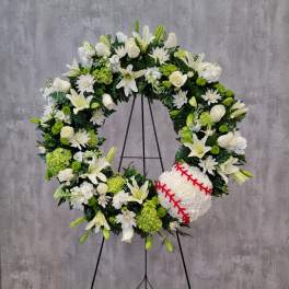 White floral wreath on a stand with a baseball at the lower right
