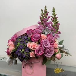 Pink and lavender roses in a pink hatbox with purple blooms