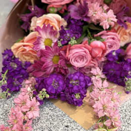Wrapped bouquet of pink and peach roses with purple and pink blooms on a granite surface