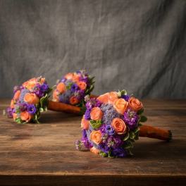 Three small bouquets of orange and purple flowers on a wooden table