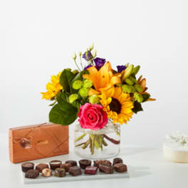 Mixed bouquet in a glass vase with a box of chocolates and a small cake.