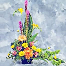 Tall asymmetrical arrangement with yellow, orange, pink, and purple flowers in a black container