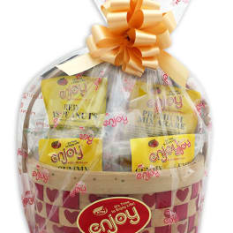 Wrapped snack gift basket with yellow packages in a heart-patterned woven basket and large peach bow