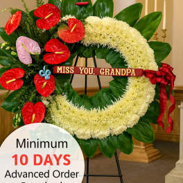 Large white sympathy wreath with red and pink flowers on a stand and a ribbon reading 'Miss you, Grandpa'