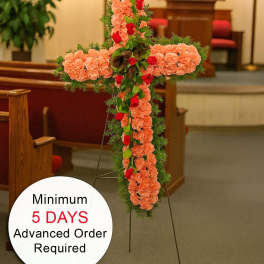 Tall peach carnation cross with red roses and greenery on an easel in a church
