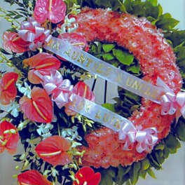 Funeral wreath with pink flowers and red tropical blooms on green leaves with white ribbons