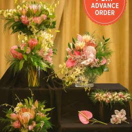 Set of pink and white tropical floral arrangements in clear glass vases on black stands.