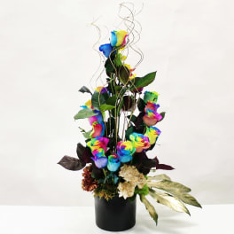 Tall arrangement of rainbow roses with cream blooms and gold accents in a black cylinder vase