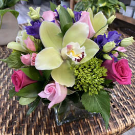 Bouquet of pink roses, purple lisianthus, and a pale orchid in a glass vase