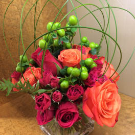 Pink and orange roses in a square glass vase with green berry accents