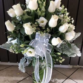 White roses and lisianthus in a glass vase with a white ribbon
