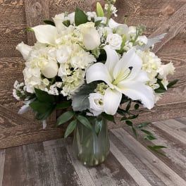 White floral arrangement with lilies, hydrangeas, and calla lilies in a glass vase